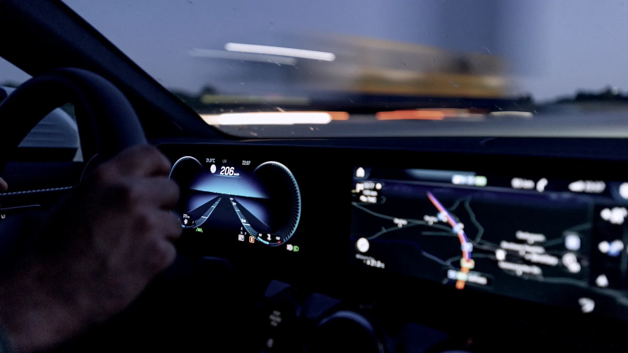 A driver's hand on the wheel, dashboard glowing at dusk