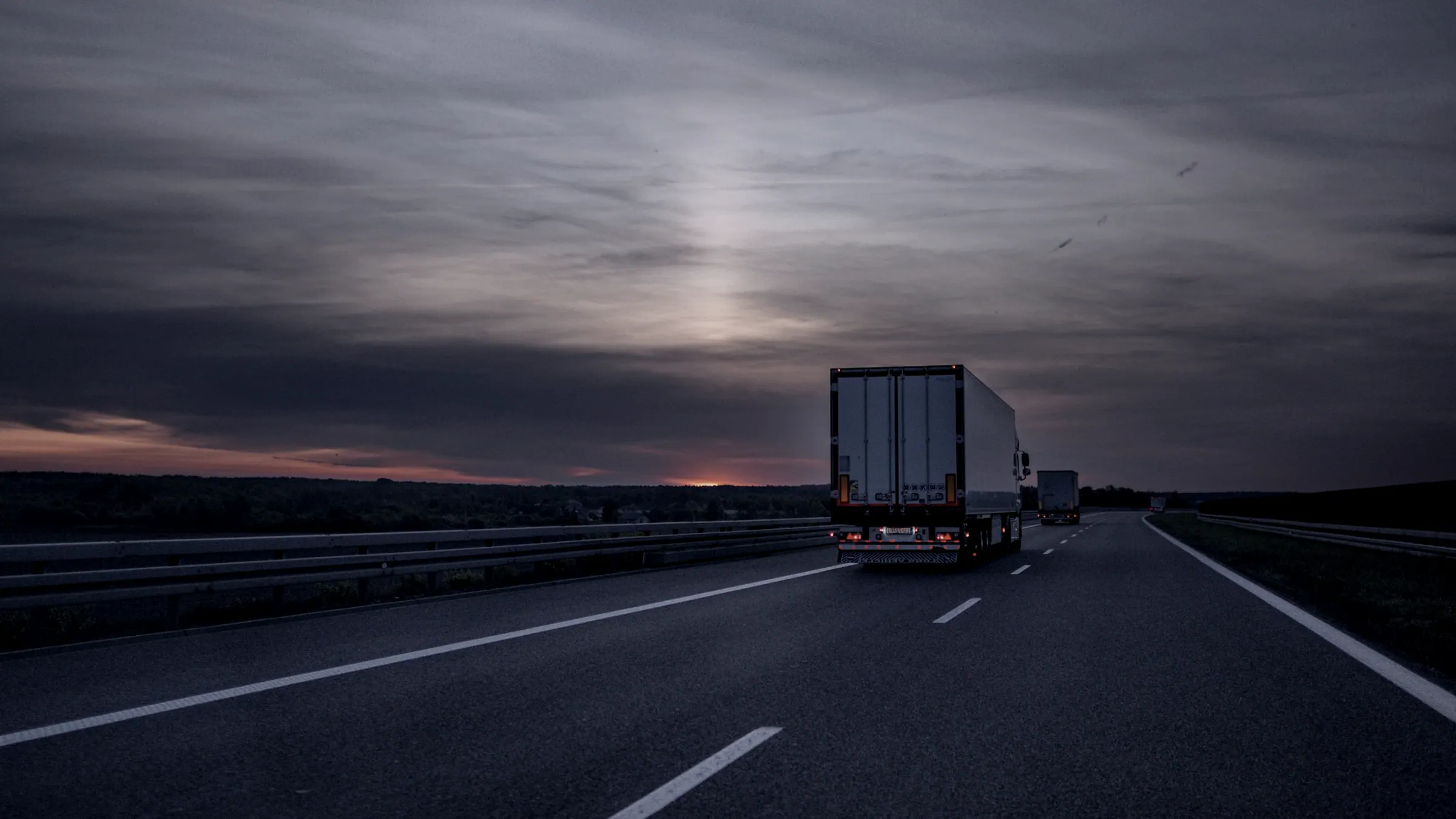 A tractor-trailer heading down an open highway at dusk